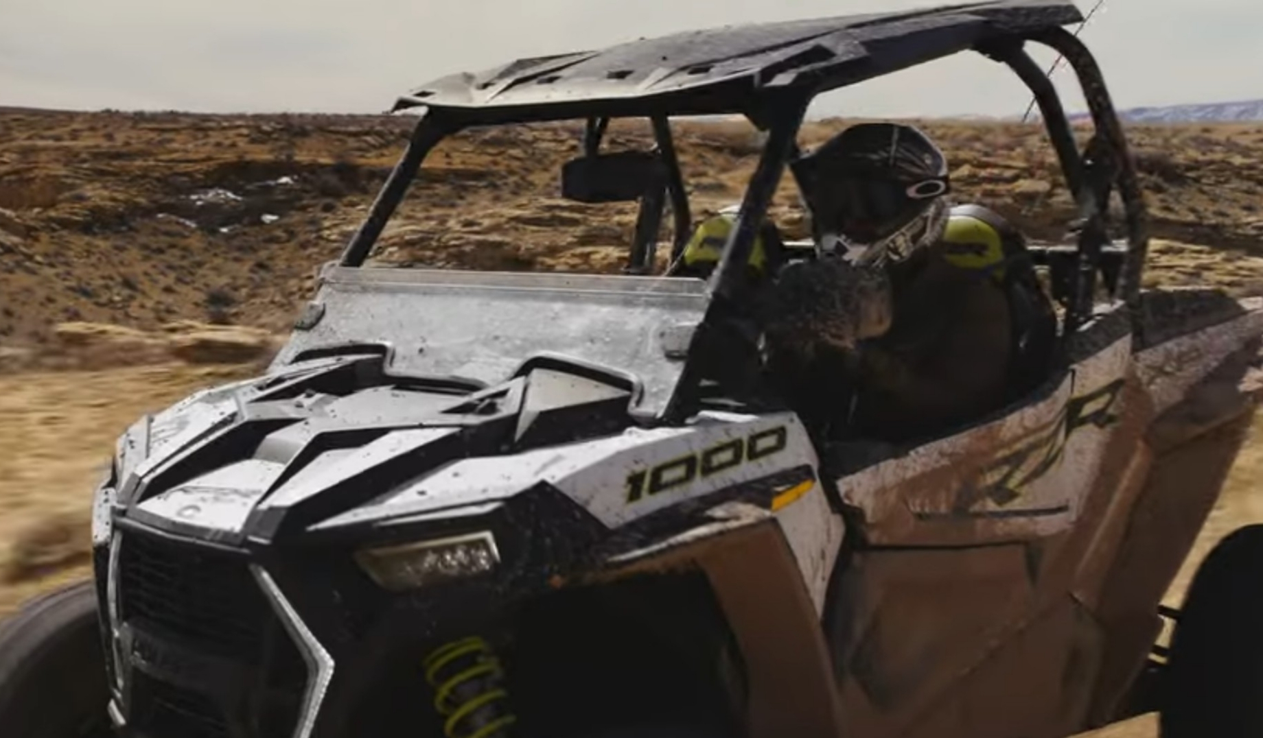 A Polaris RZR 1000 is parked on a desert field.