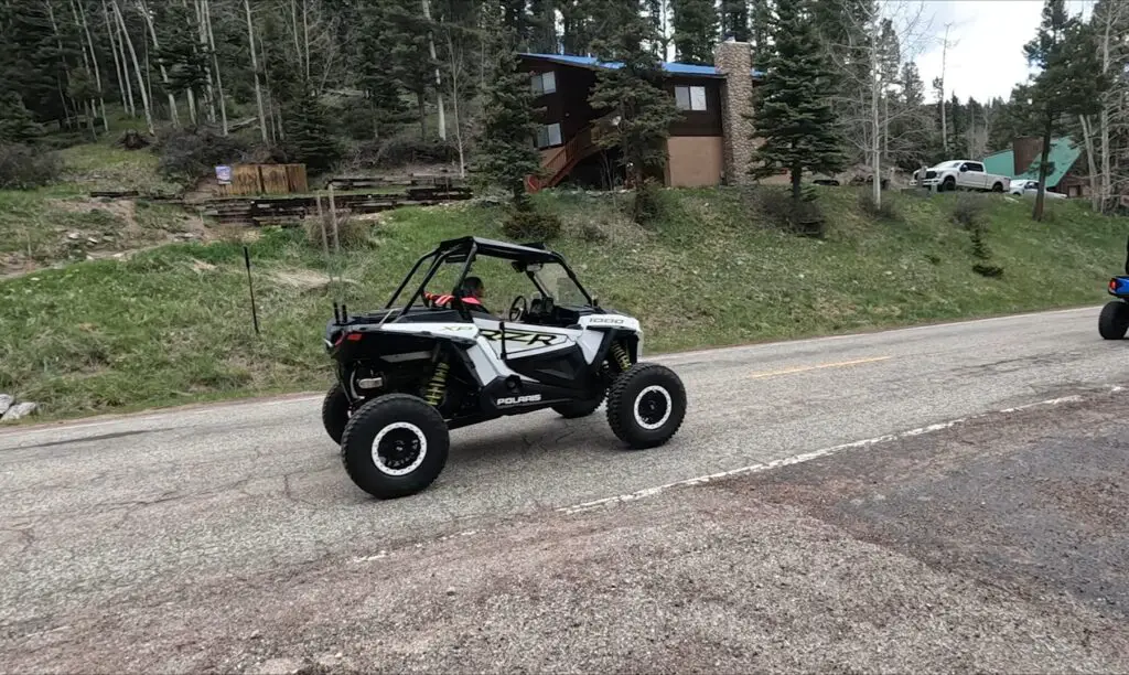 A Polaris RZR is being driven through a concrete road.