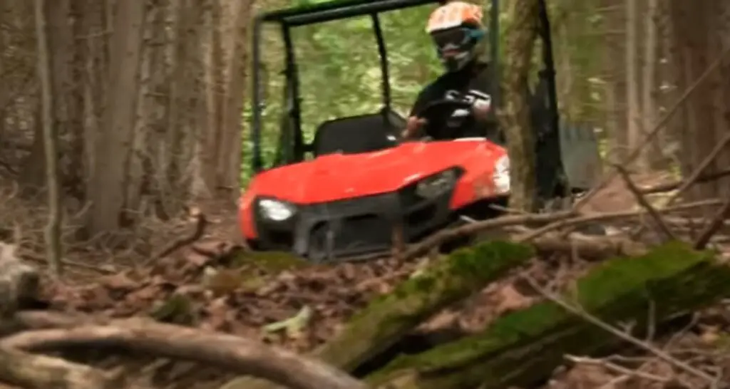 A Polaris Ranger 500 is being driven through a dry forest.