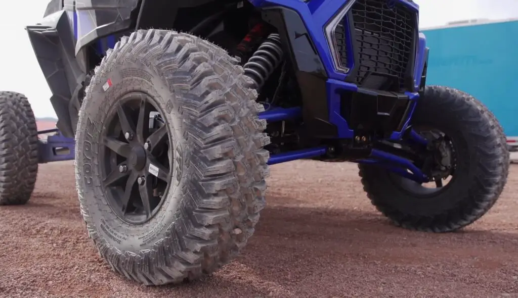 A Polaris RZR XP Turbo S is parked on a dirt surface in front of a warehouse.