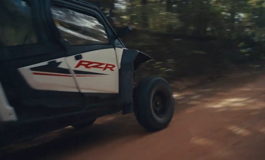 A Polaris RZR is being driven through a dirt jungle terrain.