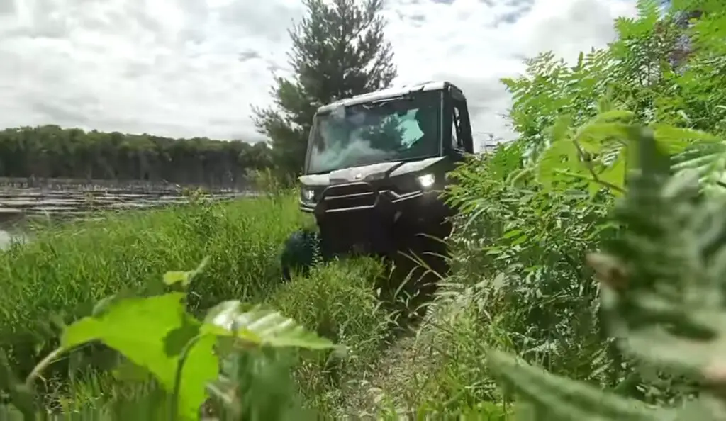 A Can-am defender HD10 is being driven through a grassy surface.