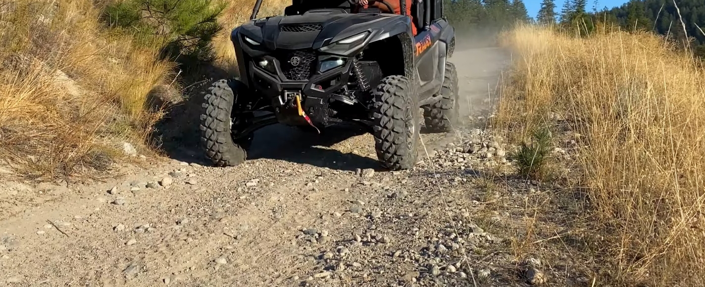 A black Yamaha UTV is being driven through a gravel road.