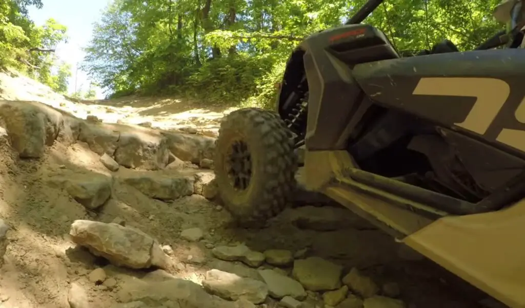 A Can-Am Maverick X3 is being driven through a gravel road.