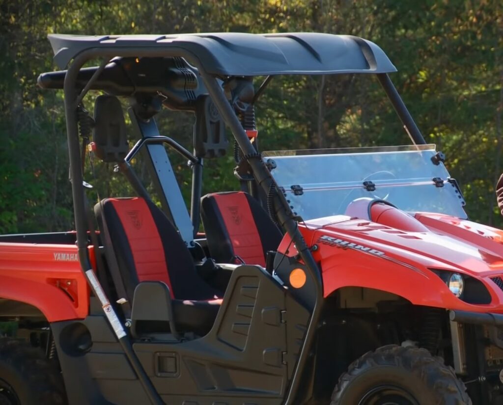 A Yamaha Rhino is parked on a grassy field. In the background there are trees and bushes.