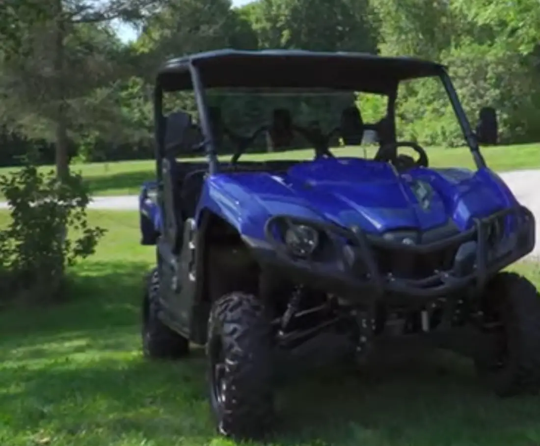 A blue Yamaha Viking EPS is parked in a garden under some trees.