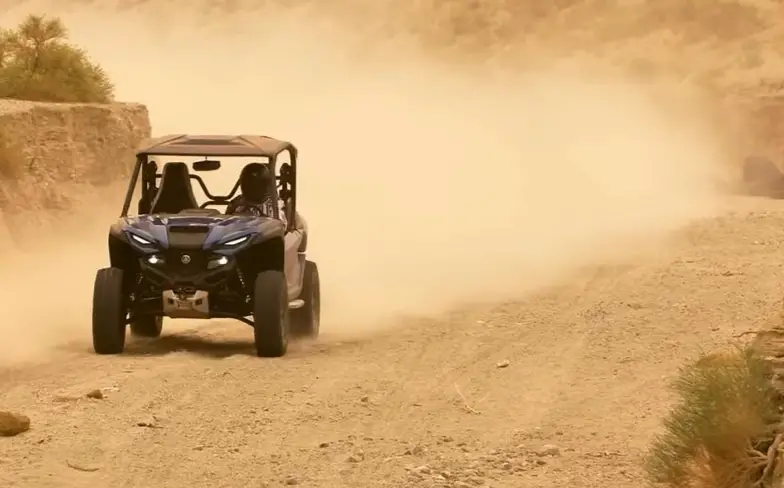 A Yamaha Wolverine RMAX2 is being driven through a dusty trail.