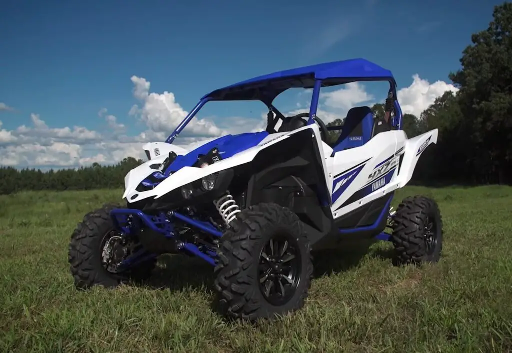 A Yamaha YXZ1000R is parked in a grass field. In the background there is beautiful blue sky.