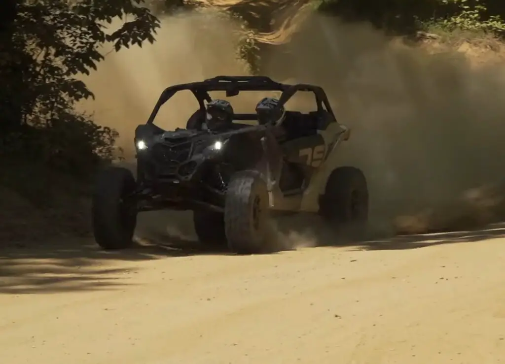 A Can-am Maverick X3 is being driven through a dusty trail.