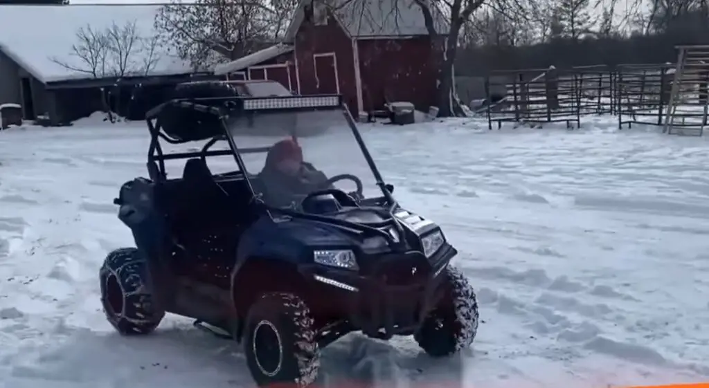 A UTV is being driven by a kid through a snow terrain.